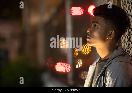 Face of sad young Asian man leaning on fence in the city streets Stock Photo