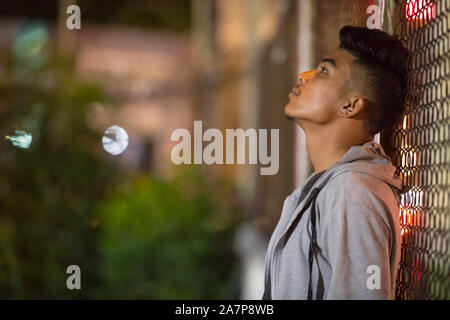 Sad young Asian man leaning on fence in the city streets at night Stock Photo