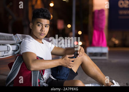 Young Asian man thinking while using phone in the city streets at night Stock Photo
