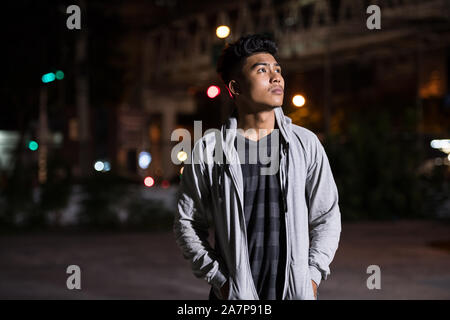 Young Asian man thinking in the city streets at night Stock Photo