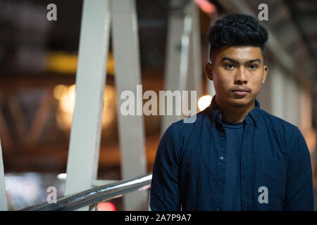 Face of young Asian man looking away on the footbridge at night Stock Photo