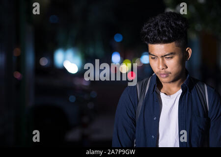 Stressed young Asian man thinking while looking down in the city streets at night Stock Photo