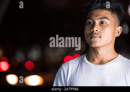 Face of young Asian man thinking in the city streets at night Stock Photo