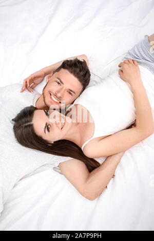 Bedtime. Young couple lying on bed top view isolated on white hugging smiling relaxed Stock Photo