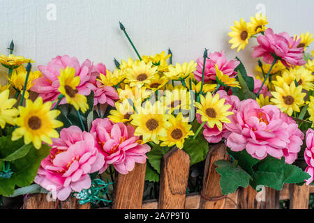 Bed of pink yellow artificial plastic flowers guarded by wooden fence Stock Photo