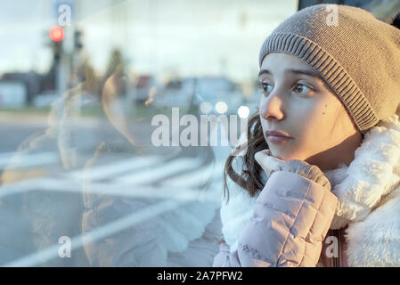 Girl teenager sits on the bus and looks out the window,teenager girl is sitting in the bus looking forward thinking. Stock Photo