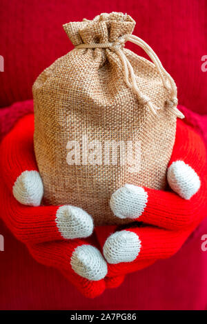 Christmas gifts bag in female hands. Red knitted gloves and a sweater. Stock Photo