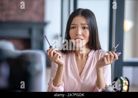 Beauty blogger choosing between two lip glosses Stock Photo