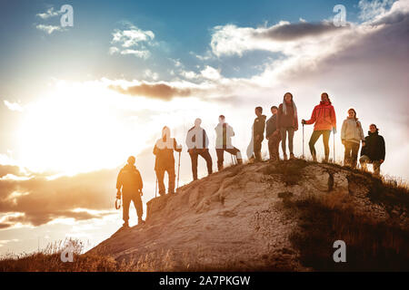 Big group of hikers stands against sunset. Hiking or trekking concept