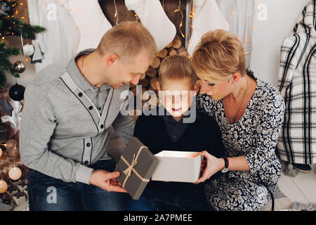 Parents and kid opening Christmas present.many gift boxes and fir trees in snow. Stock Photo