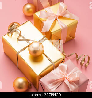 Gifts decorated with various boxes with satin ribbon bows. Golden toy balls on a pastel pink background. Holiday concept. Square frame Stock Photo