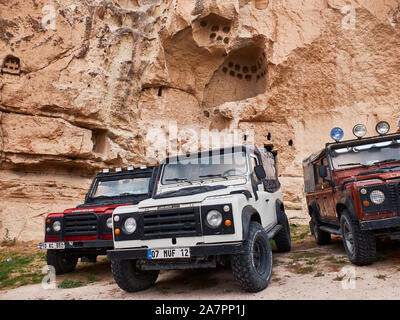 Goreme, Turkey - October 2019. Three Land Rover offroad cars park in front of typical cappadocian cave house remains. Stock Photo