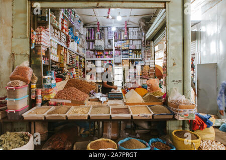 Rissani, Morocco - September 18th, 2019: Traditional stall with spices and herbs, with seller using a ladder to place products, at the food market of Stock Photo
