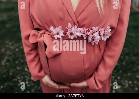 Beautiful pregnant women in pink outfit photographed next to blossom tree in the spring. close up photo of her belly and no face shown. Stock Photo