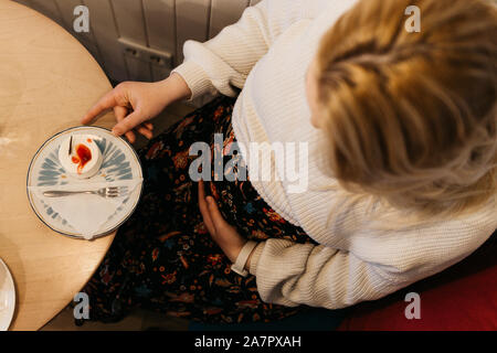 Portrait of beautiful pregnant woman eating cake in the restaurant. She is holding her belly with one hand. Stock Photo