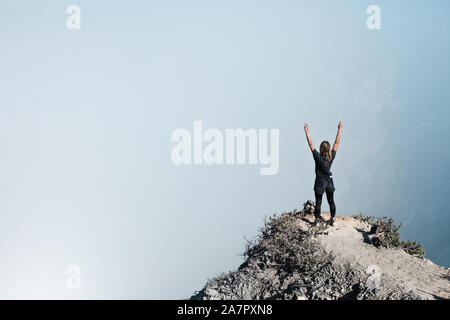 Young woman have fun on summit of active volcano. Stand on high cliff above crater acid lake with poisonous fume. Popular travel destination. Stock Photo