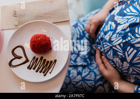 Portrait of beautiful pregnant woman eating cake in the restaurant. She is holding her belly with one hand. Stock Photo