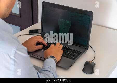 Developer coding on a laptop and creating a artificial intelligence software. Human like face made out of code appearing on the screen. Stock Photo