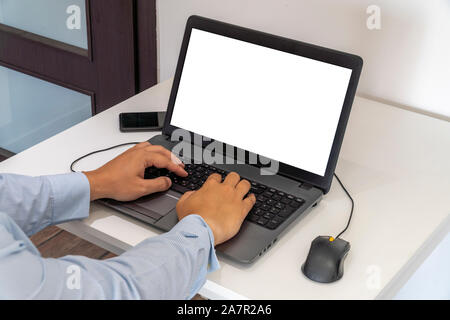 Person working on a laptop in a business office enviroment. Over the shoulder shot of man typing on a computer with blank screen. Stock Photo