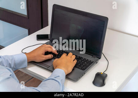 Developer coding on a laptop and creating a artificial intelligence software. Human like face made out of code appearing on the screen. Stock Photo