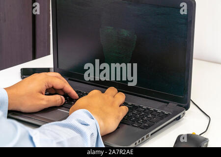 Developer coding on a laptop and creating a artificial intelligence software. Human like face made out of code appearing on the screen. Stock Photo