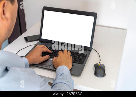 Person working on a laptop in a business office enviroment. Over the shoulder shot of man typing on a computer with blank screen. Stock Photo