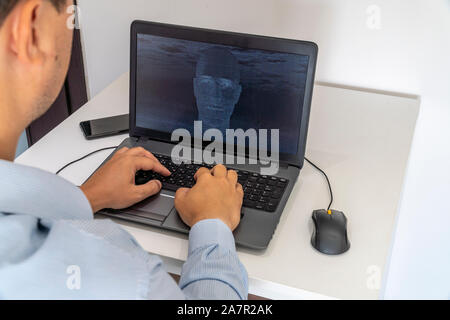 Developer coding on a laptop and creating a artificial intelligence software. Human like face made out of code appearing on the screen. Stock Photo