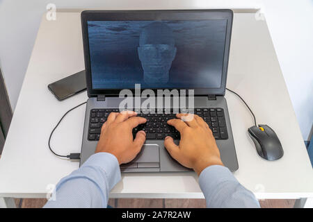 Developer coding on a laptop and creating a artificial intelligence software. Human like face made out of code appearing on the screen. Stock Photo