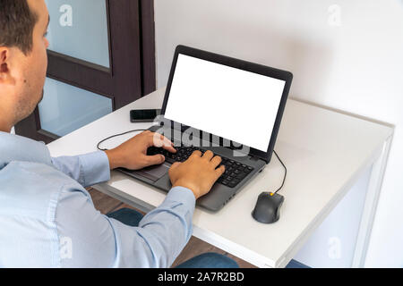 Person working on a laptop in a business office enviroment. Over the shoulder shot of man typing on a computer with blank screen. Stock Photo