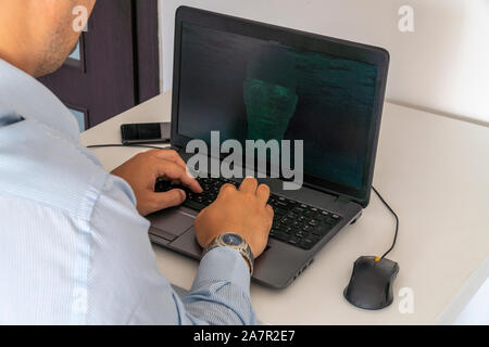 Developer coding on a laptop and creating a artificial intelligence software. Human like face made out of code appearing on the screen. Stock Photo