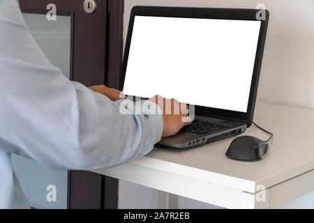 Person working on a laptop in a business office enviroment. Over the shoulder shot of man typing on a computer with blank screen. Stock Photo