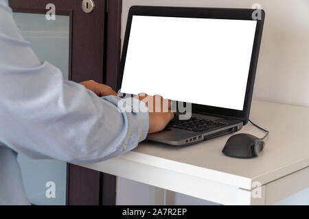 Person working on a laptop in a business office enviroment. Over the shoulder shot of man typing on a computer with blank screen. Stock Photo