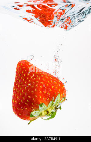 Strawberry falls deeply under water with a big splash. Fruit sinking in clear water on white background Stock Photo