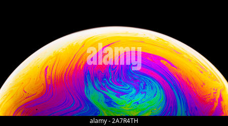 Rainbow soap bubble on a dark background. Close-up of colorful surface. Stock Photo