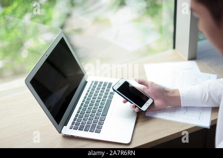 View of the hand of businessman using a smartphone at a desk with a laptop in an office Stock Photo