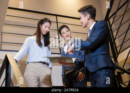 Group of three male and female smiling young businesspeople discussing a document held by one of them on a staircase in an office Stock Photo