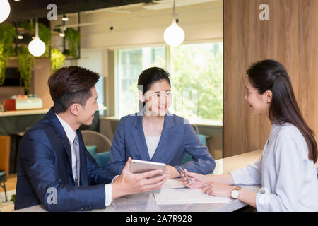 Group of three young female and male smiling businesspeople talking in an office with one of them holding a digital tablet Stock Photo