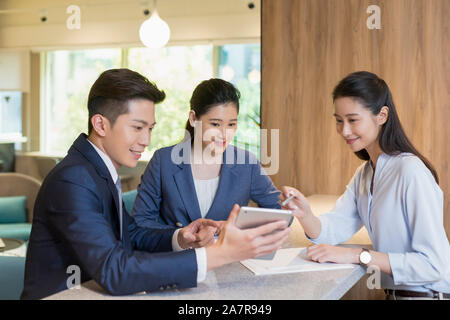 Group of three male and female young smiling businesspeople sitting together in an office and looking at a digital tablet held by one of them Stock Photo
