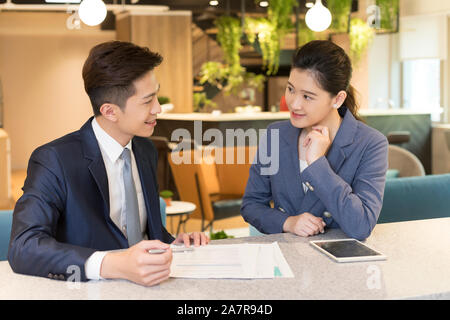 Two young smiling male and female businesspeople talking about a document in an office Stock Photo