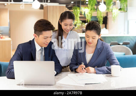 Photograph of group of three male and female young businesspeople looking together at a document while working in an office Stock Photo