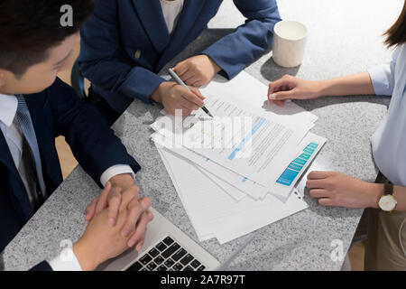 High angle view photograph of group of three male and female businesspeople looking together at a document while working in an office Stock Photo