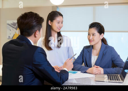 Photograph of three male and female young smiling businesspeople talking together in an office Stock Photo