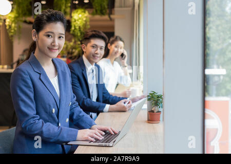 Portrait of three smiling young male and female businesspeople looking at the camera while sitting at a desk in an office Stock Photo