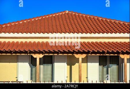 Sloped light brown clay tile roof of a rural traditional one-story house in southern Greece is covered with brown tiles against a blue sky. Stock Photo