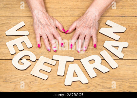 word vegetarian laid out next to female old hands lying on a wooden table Stock Photo