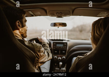 Beautiful couple doing a car trip on countryroad, view from rear seat. Stock Photo