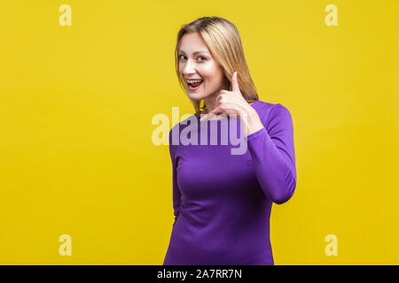 Call me back! Portrait of playful attractive woman in elegant tight purple dress doing talking on phone gesture, smiling and flirting at camera. indoo Stock Photo