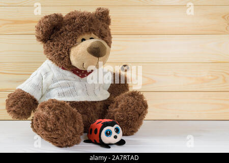 toy brown teddy bear sits on a white wooden table on a background of wooden boards Stock Photo