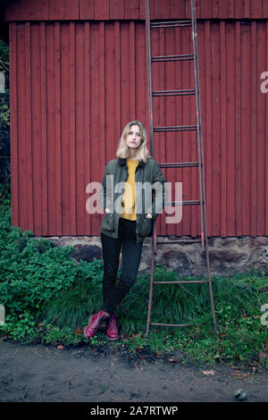 Blonde woman leaning on ladder that is propped on a red barn Stock Photo