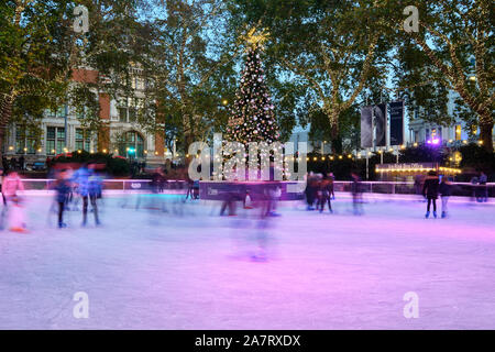Movement Blur image of people skating on Christmas decorated Ice Rink at the London Natural History Museum at Dusk, around the central xmas tree. Stock Photo